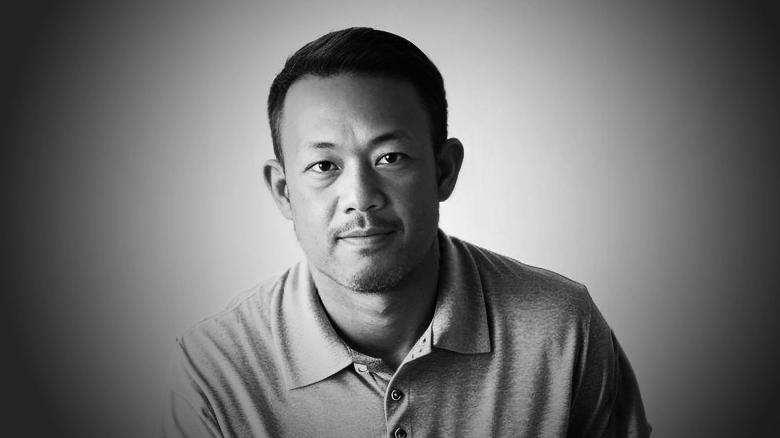 Black and white portrait of a man in a polo shirt against a gradient background.