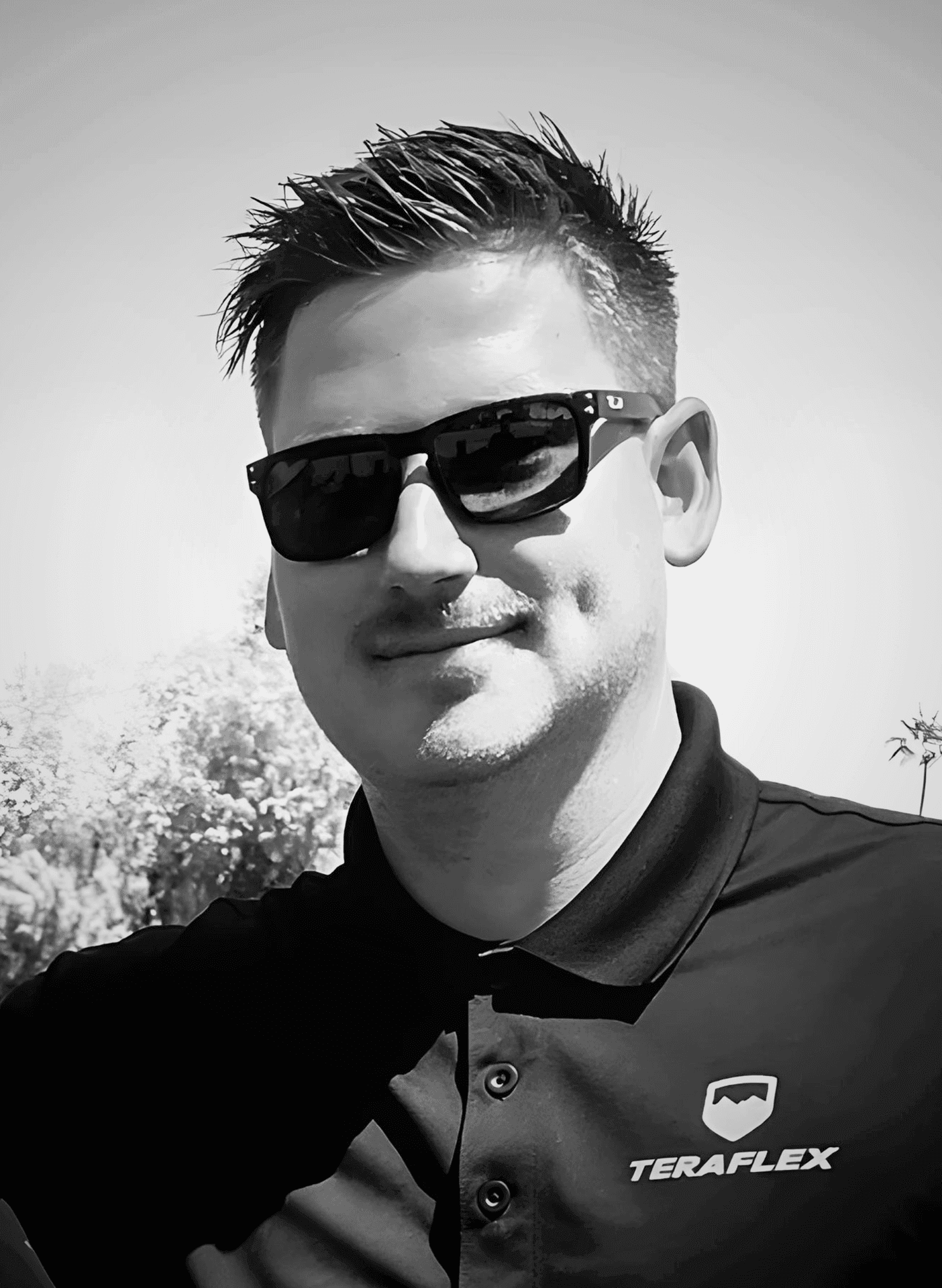 Black and white portrait of a person wearing sunglasses and a collared shirt outdoors.